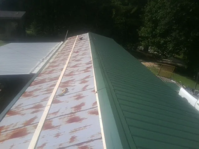 Old rusted panels beside newly installed green metal roofing — Wind Damage Roof Repair by Roofing Brothers in West Newton