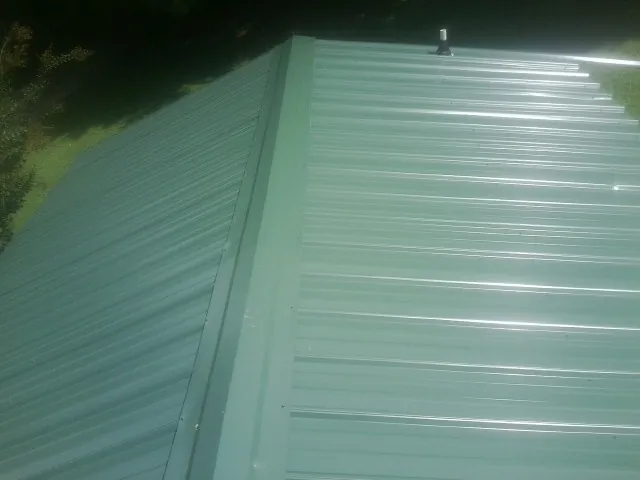 New green metal panels meeting at the ridge of a roof — Flat Roof Repair work by our crew in West Newton
