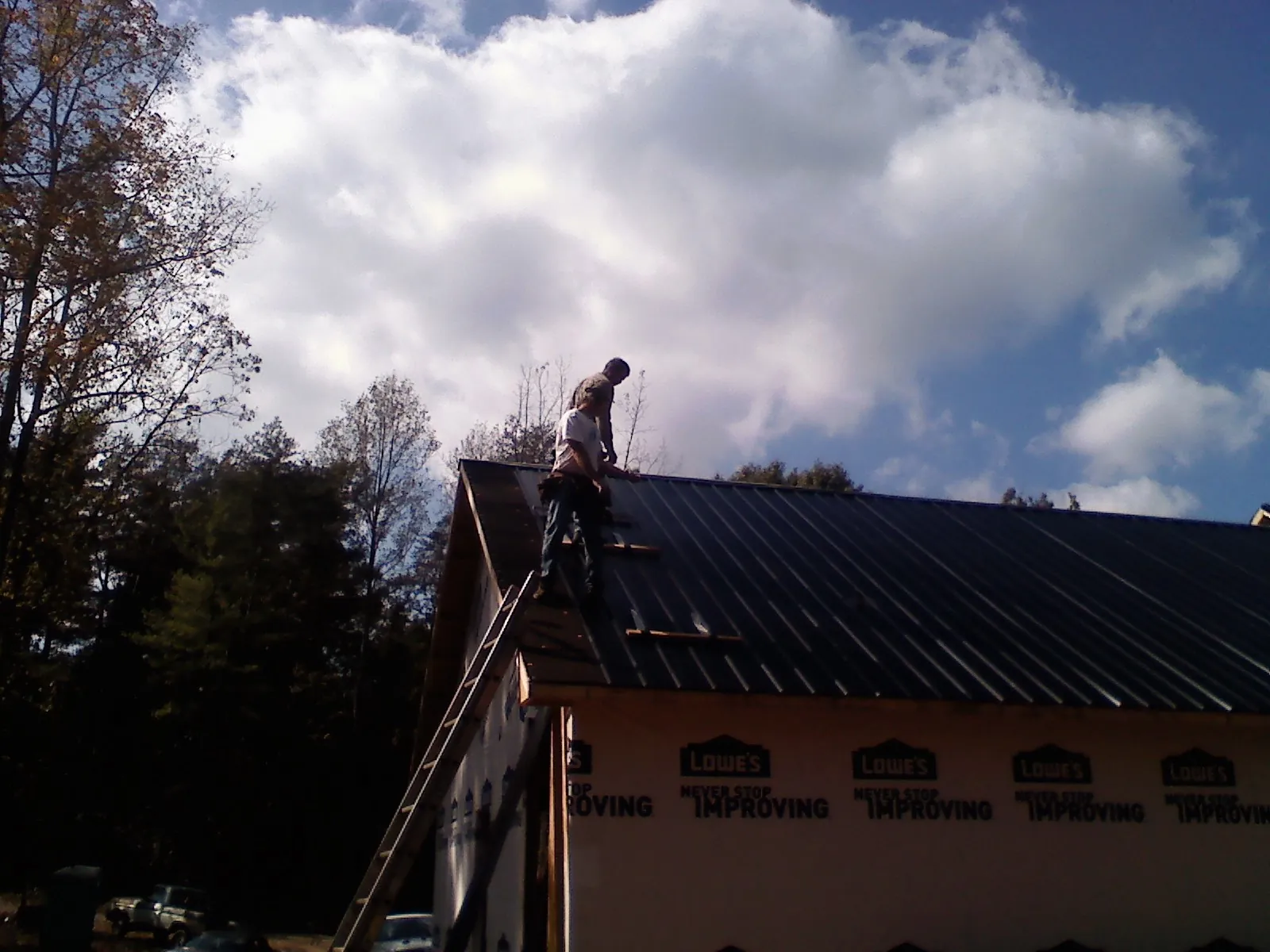 Roofer fastening dark metal panels high against a cloudy sky, from a Roof Inspection job in West Newton