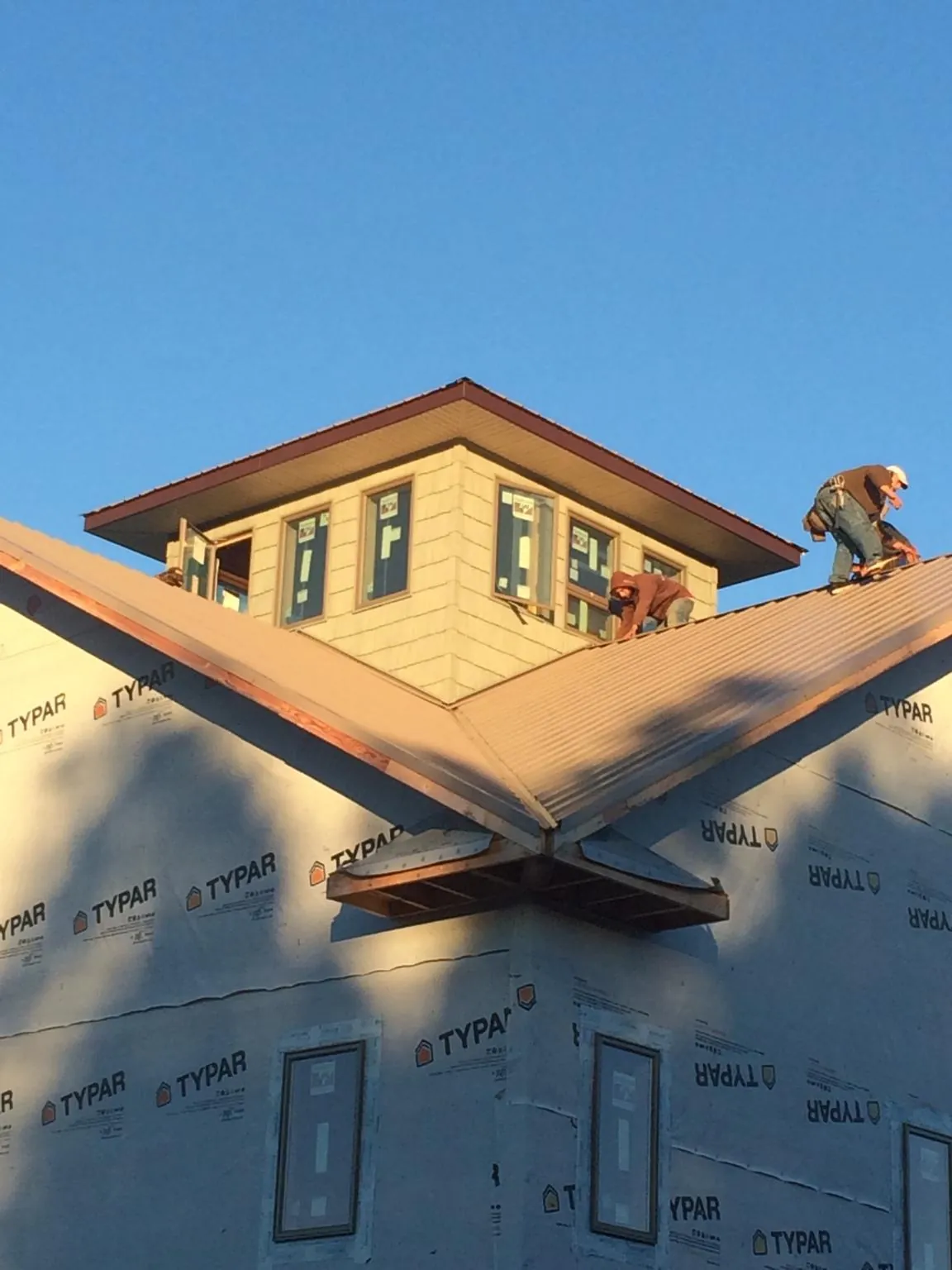 Roofers working around a rooftop cupola on a new metal roof at sunset in West Newton
